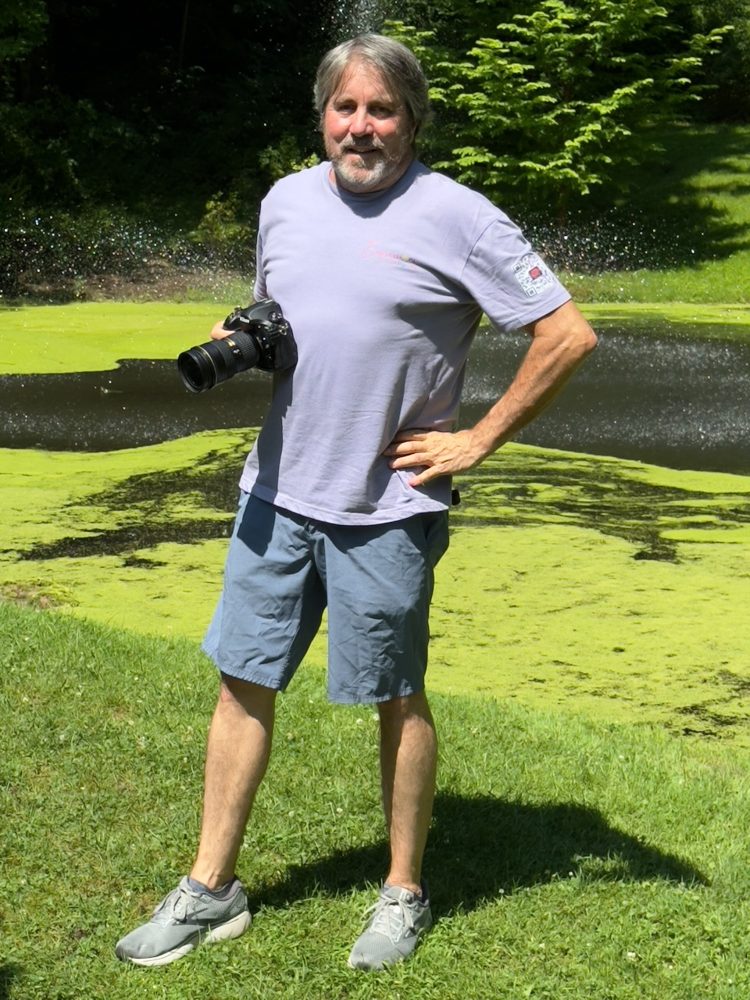 Chris Austermann standing by a pond holding his camera